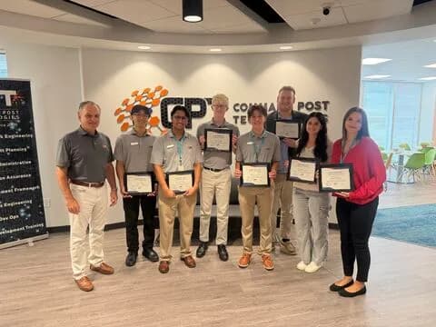 Eight people holding framed certificates in front of a Command Post Technologies logo on an office lobby wall.