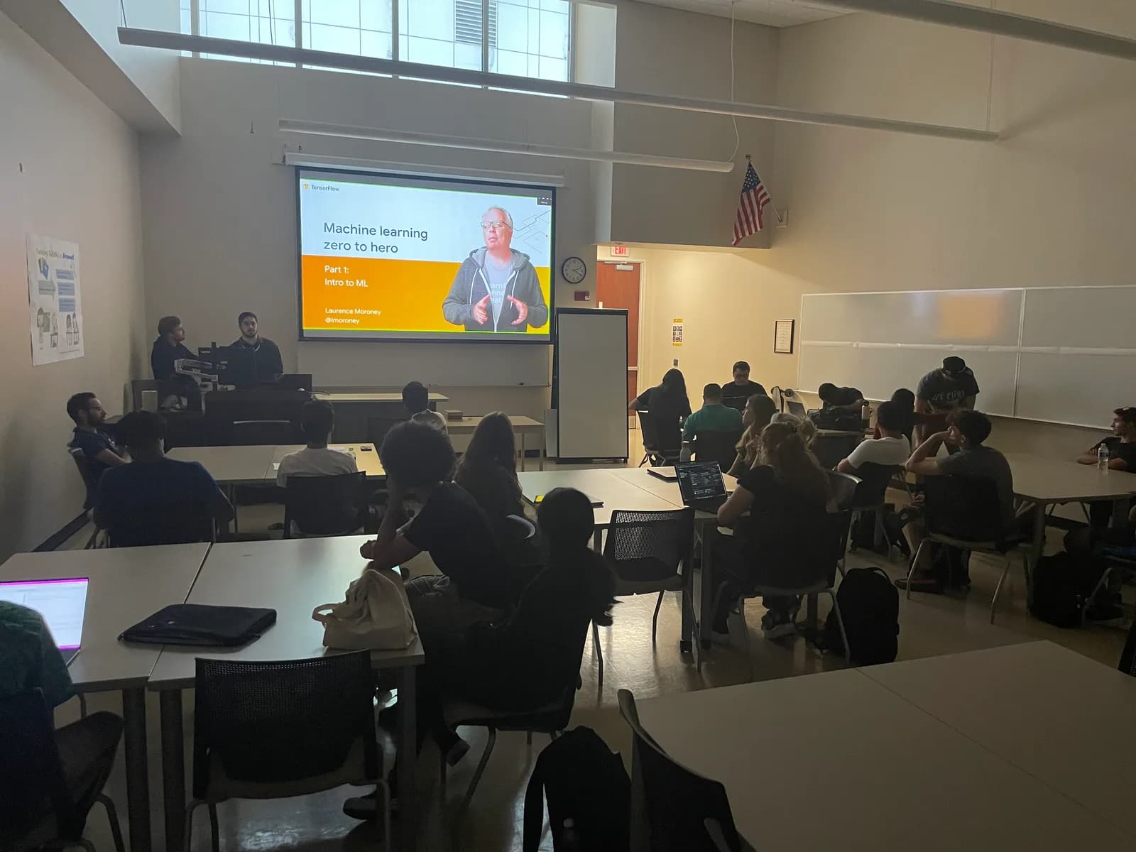 Students seated at classroom tables watching a projected TensorFlow slide reading 'Machine learning zero to hero — Part 1: Intro to ML' at the first Project Kestrel meeting.