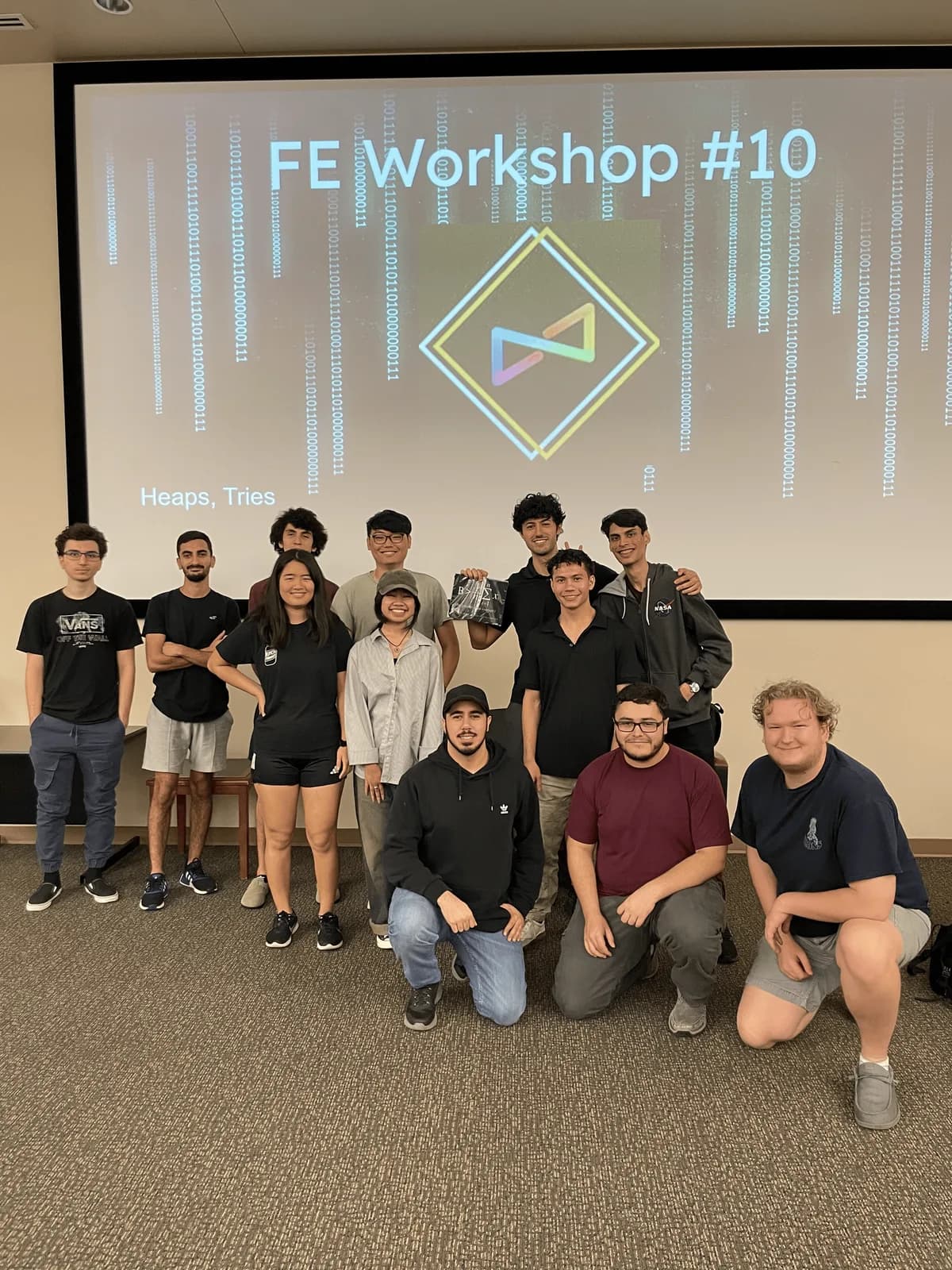 Twelve students posing in front of a projected slide reading 'FE Workshop #10 — Heaps, Tries' after a review session.